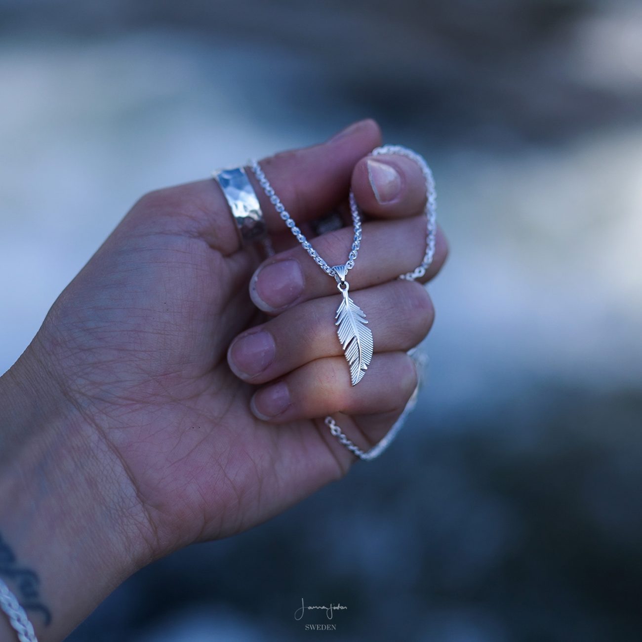 A hand is holding a Sterling silver feather necklace with pendant