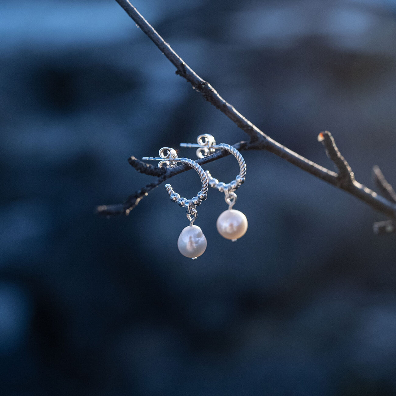 A pair of handcrafted sterling silver pearl earrings with genuine freshwater pearls hanging in a tree