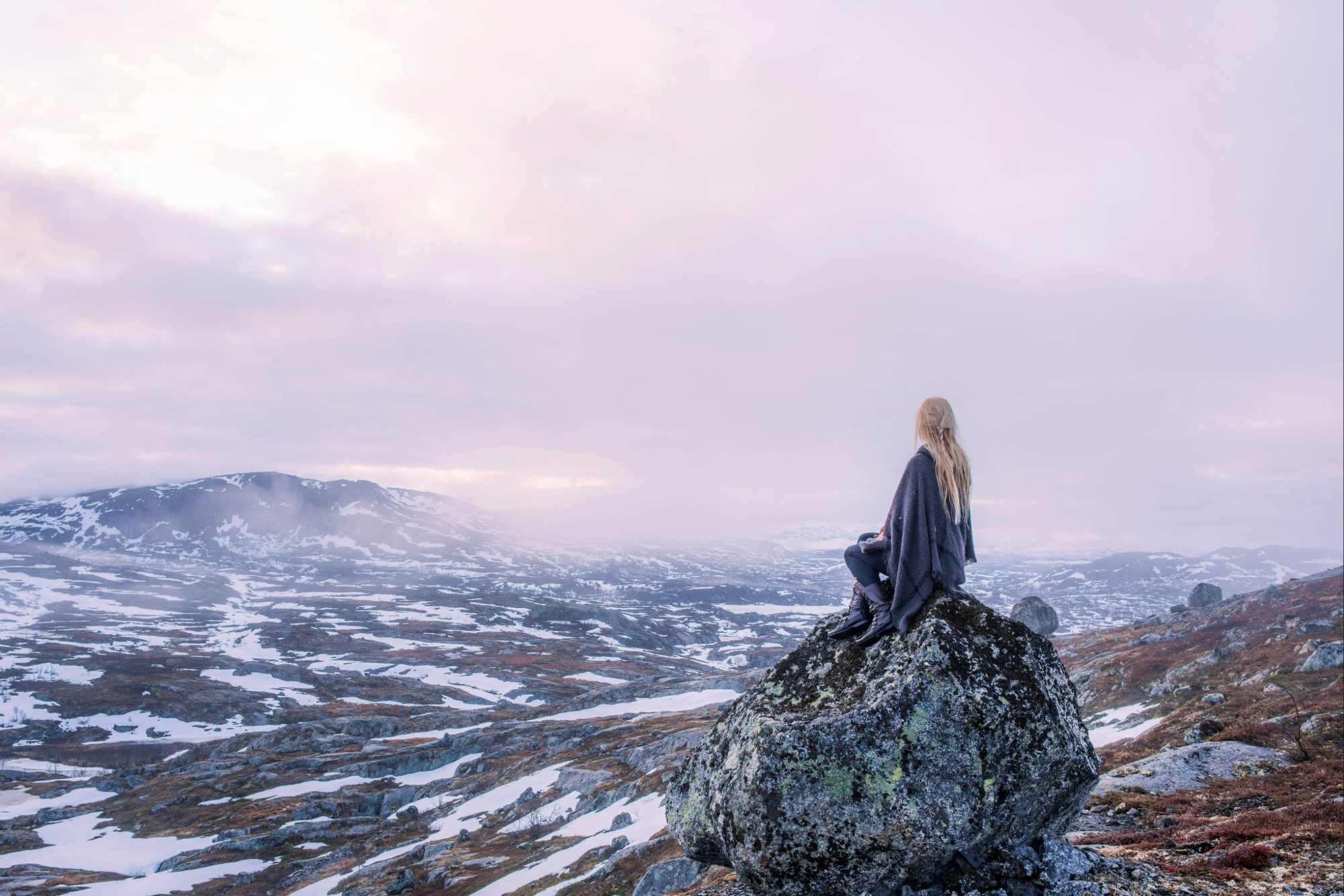 A woman sitting on a rock looking over a snowy nordic landscape