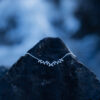 A silver leaf necklace with delicate leaf details laying on a dark rock