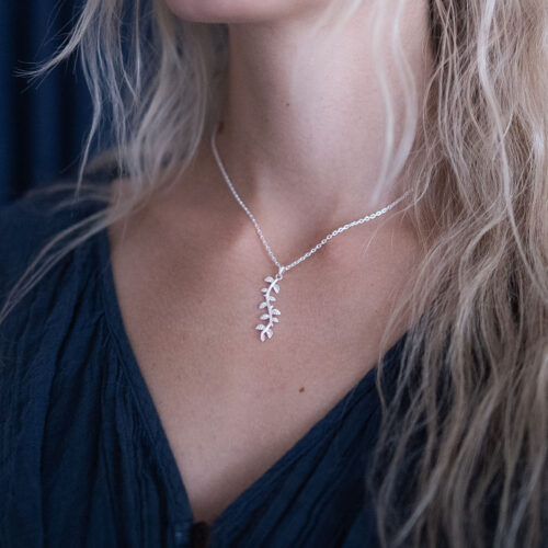 A woman wearing a silver leaf pendant necklace on her neck