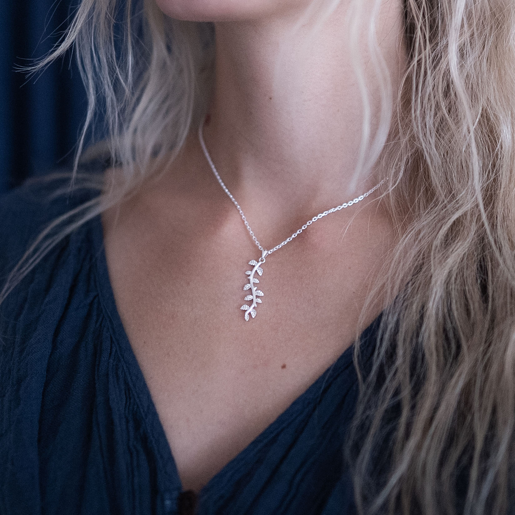 A woman wearing a silver leaf pendant necklace on her neck