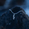 A silver leaf pendant necklace with delicate botanical details laying on dark rock