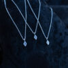 Three silver rune necklaces with different runes laying on a dark rock